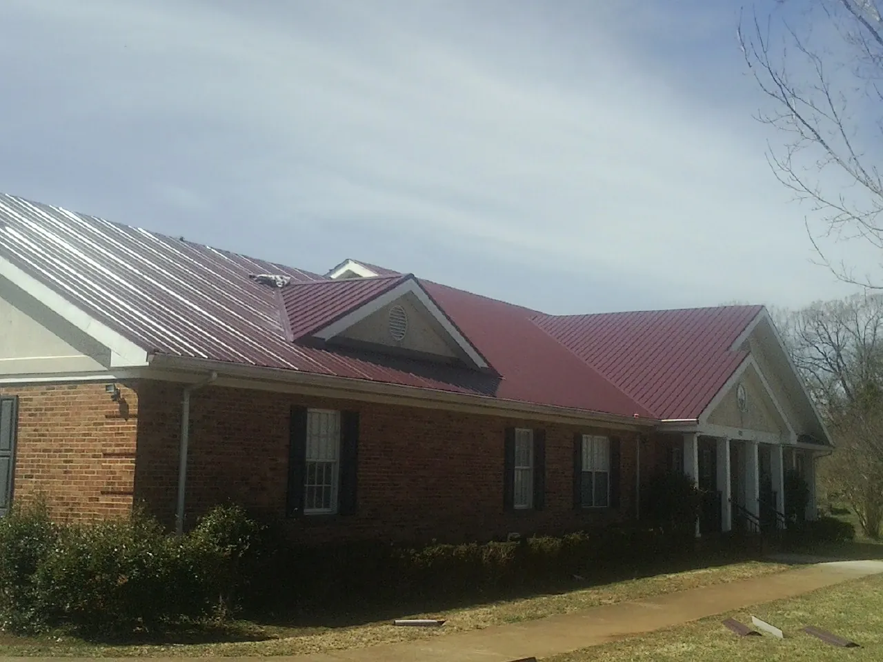 Red metal roof with gabled entries on a long brick building, from a Hail Damage Roof Repair job in Central City