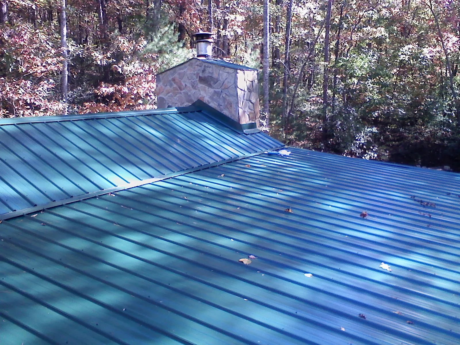 New green metal roof and stone chimney surrounded by autumn woods in Central City