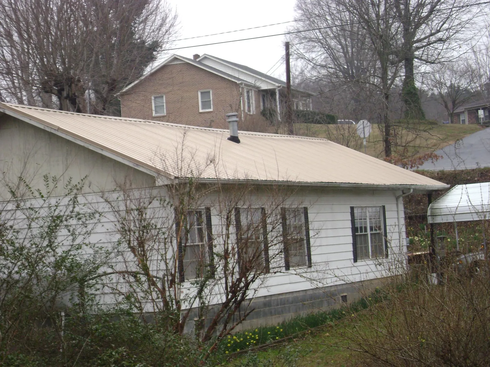 Tan metal roof on a white sided house set into a hillside — Commercial Roofing by Roofing Brothers in Central City